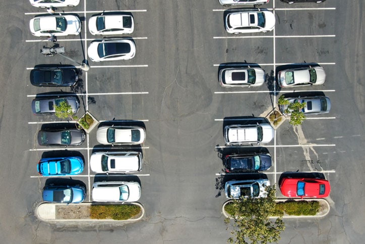 Aerial top view of parking lot at shopping mall with varieties of colored vehicles. People walking to their car and trying to park.