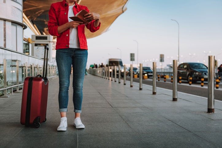 Cropped portrait of lady in red jacket holding airline ticket while standing on the street