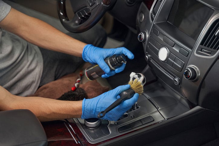 Cropped image of service worker hands in protective gloves, washing car dashboard with brush and detergent during detailing