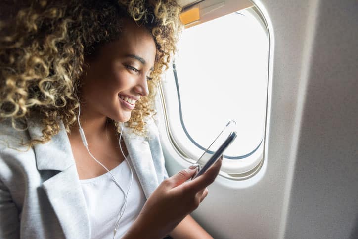 Woman Sitting Near Window on Airplane Looking At Phone