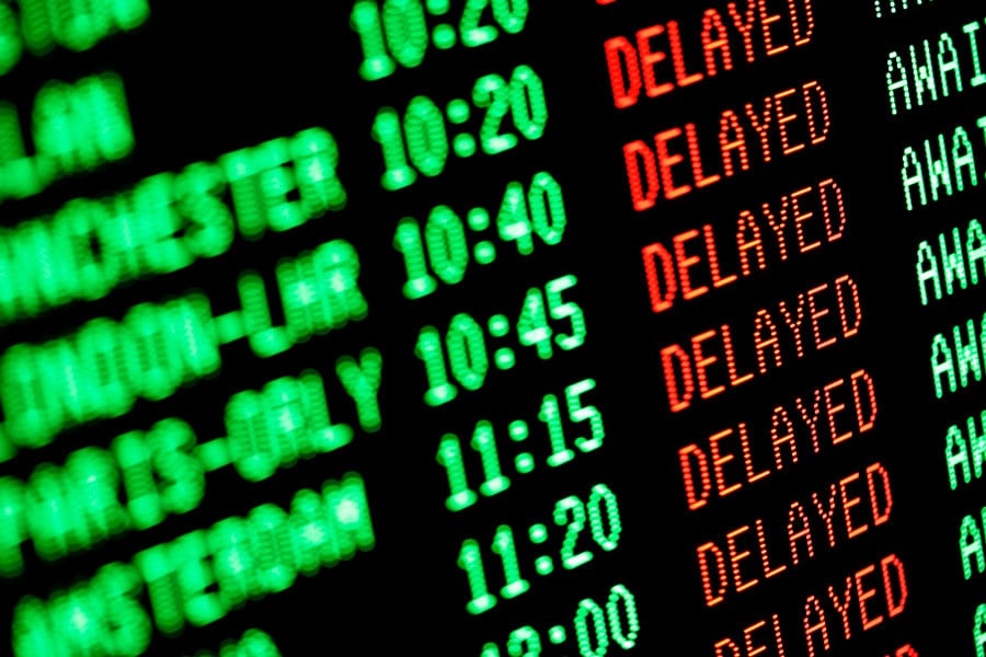 Digital airport flight information board showing a list of flights marked as delayed in red text, serving as a reminder to check your travel advice.
